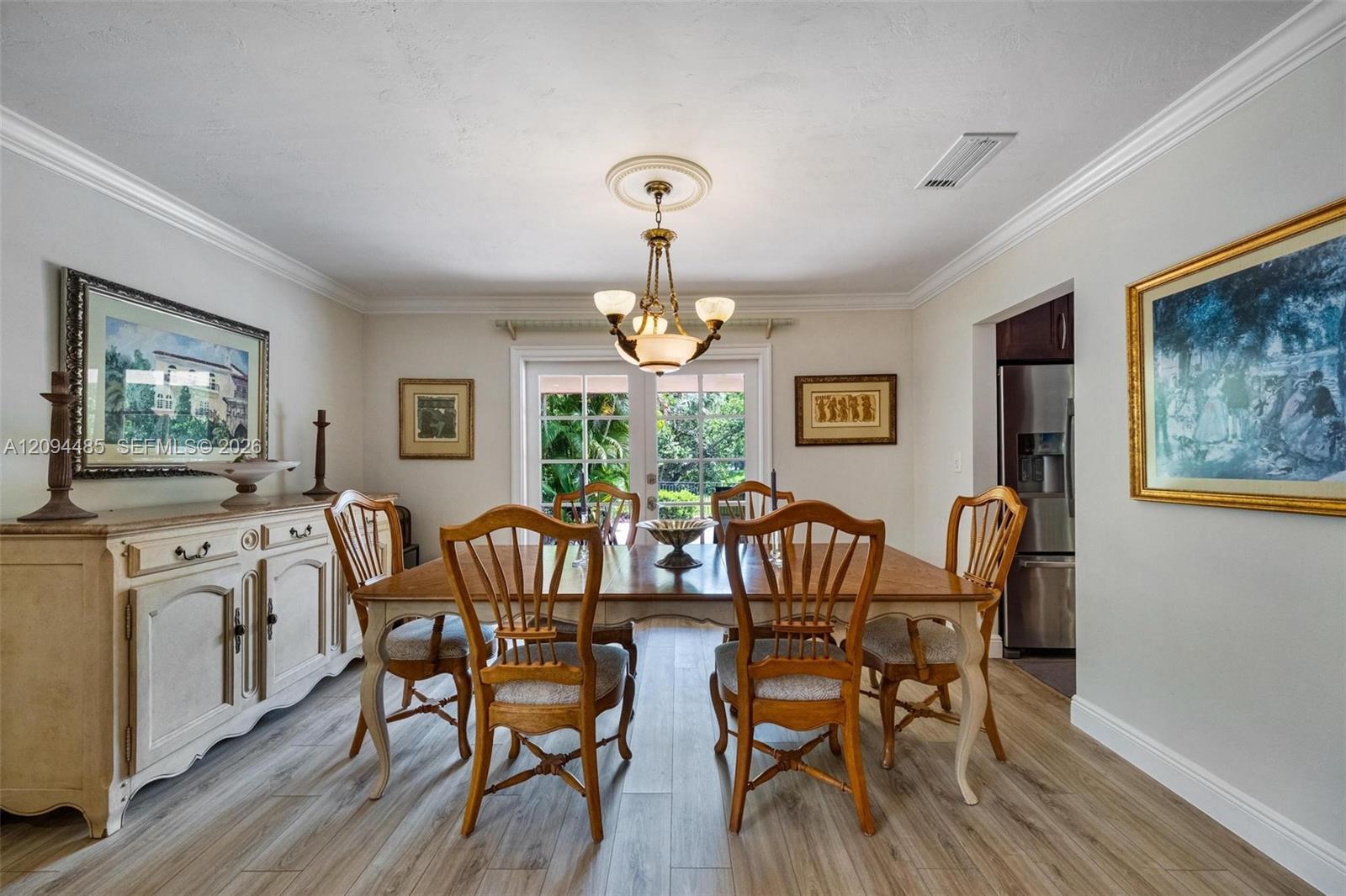 Dining space featuring wood-finish flooring, crown molding, a central multi-light chandelier with a ceiling medallion, and glass-paneled French doors