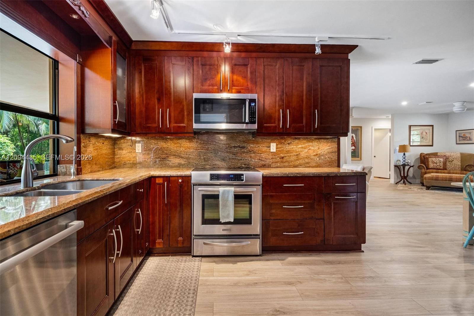 Kitchen featuring dark wood cabinetry, stainless steel appliances, stone countertops, stone backsplash, and track lighting