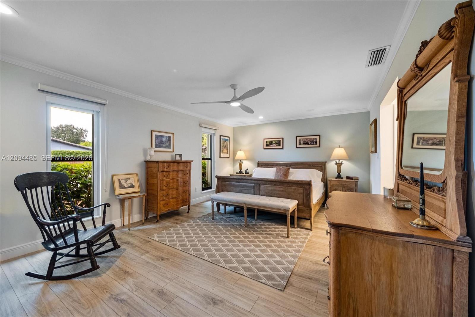 Room featuring wood-finish flooring, a modern three-blade ceiling fan, crown molding, and dual windows with roller shades