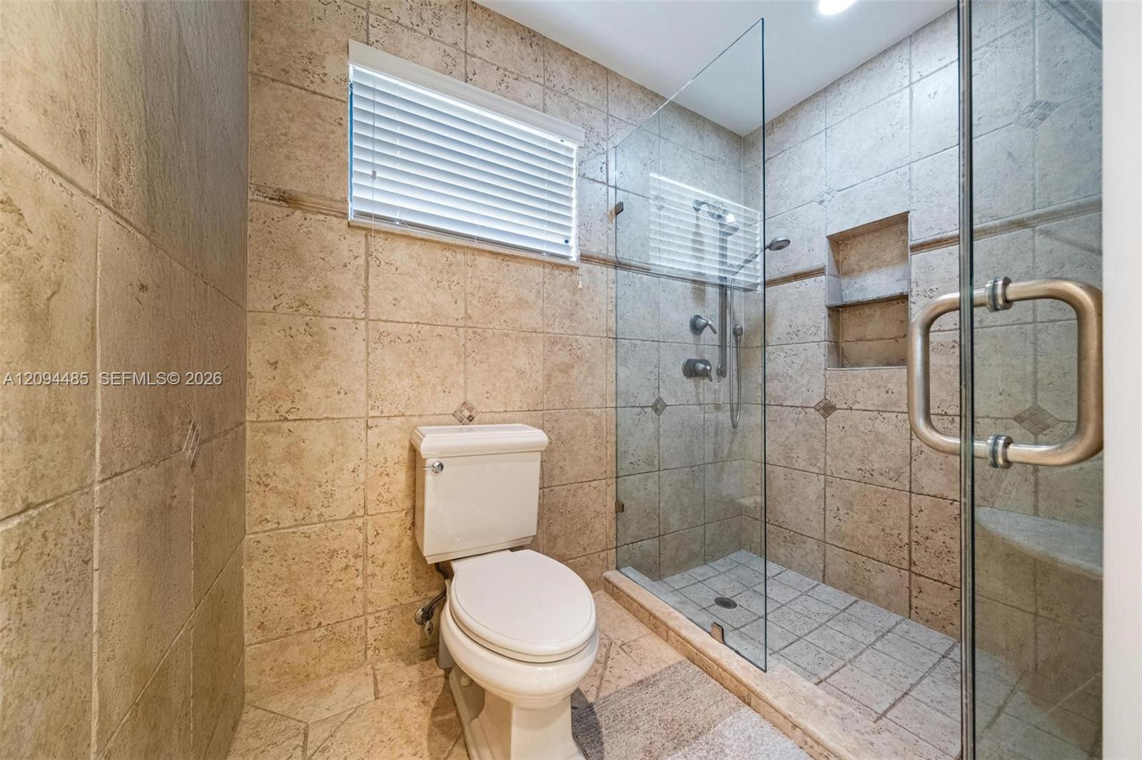 Walk-in shower featuring glass enclosure, built-in recessed shelving, wall-mounted shower head, and tile surround with integrated tile flooring