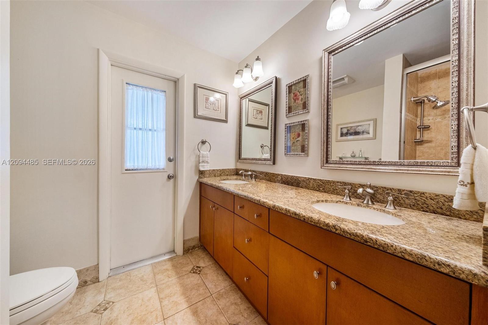 Dual-sink vanity featuring wood-finish cabinetry, stone countertops, integrated oval basins, and framed wall mirrors
