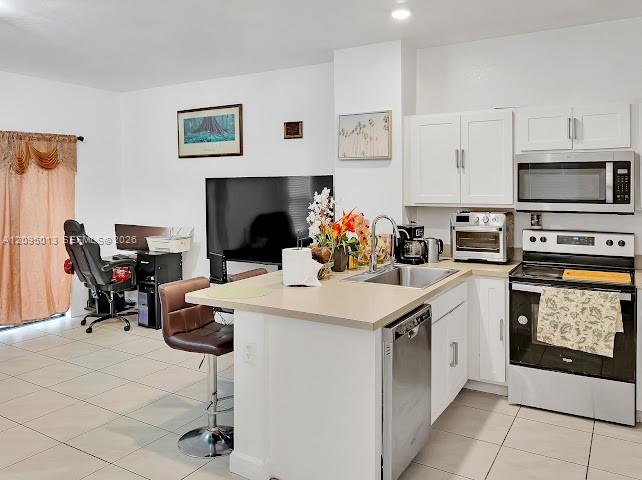 Kitchen featuring white shaker-style cabinetry, solid-surface countertops, a stainless steel undermount sink with a gooseneck faucet, and tile flooring