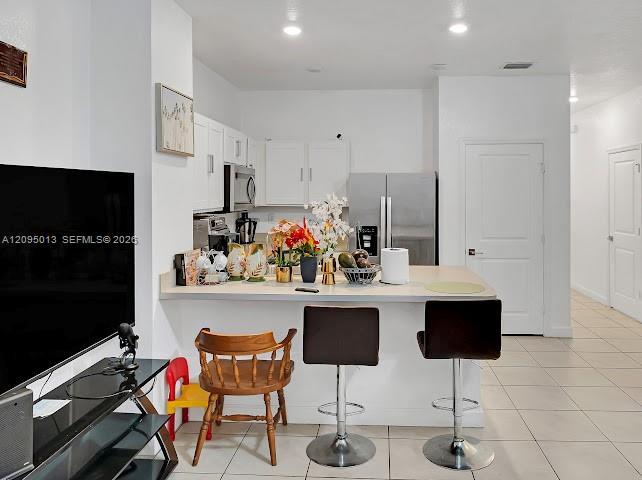 Kitchen featuring white cabinetry, solid-surface breakfast bar, recessed lighting, and stainless steel appliances