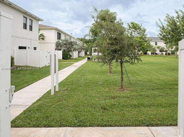 Common green space featuring a concrete pedestrian walkway, mature landscaping, and white privacy fencing