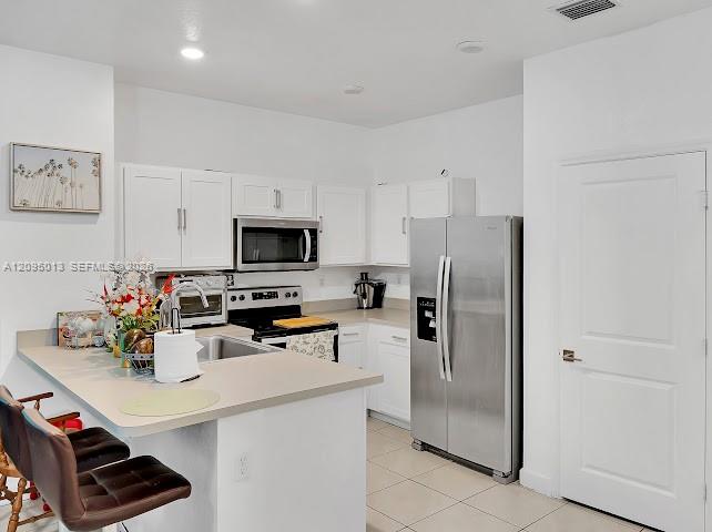 Kitchen featuring white shaker-style cabinetry, a stone-composite countertop with a breakfast bar, stainless steel appliances, and tile flooring