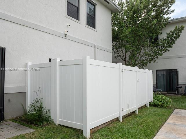 White vinyl privacy fencing, stucco exterior cladding, and paved stone walkway