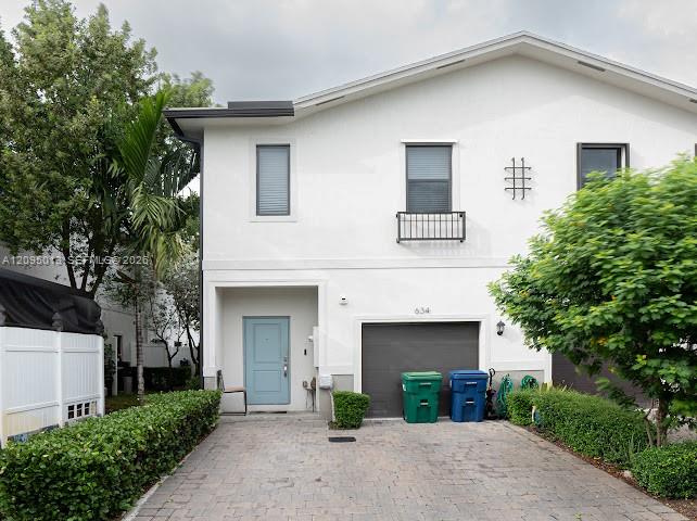 Two-story exterior featuring a light-toned stucco facade, a stone paver driveway, an attached garage, a window box, and a solid-panel front door