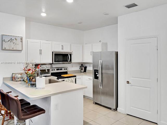 Kitchen featuring white cabinetry, solid-surface countertops, stainless steel appliances, recessed lighting, and tile flooring