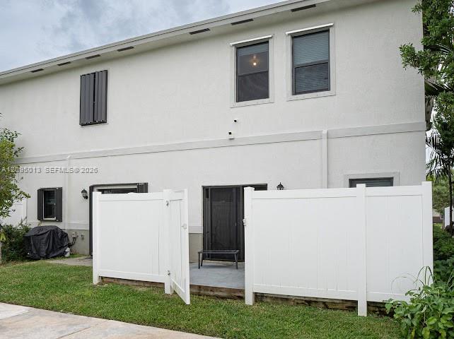 Stucco exterior featuring dual-story windows, privacy-fencing, and a concrete patio