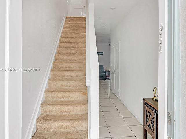 Entryway featuring neutral-tone carpeting on stairs, white painted handrail, ceramic tile flooring, and recessed ceiling lighting