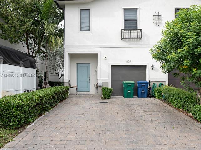 Stucco exterior featuring a paver driveway, an attached garage, and manicured privacy hedging