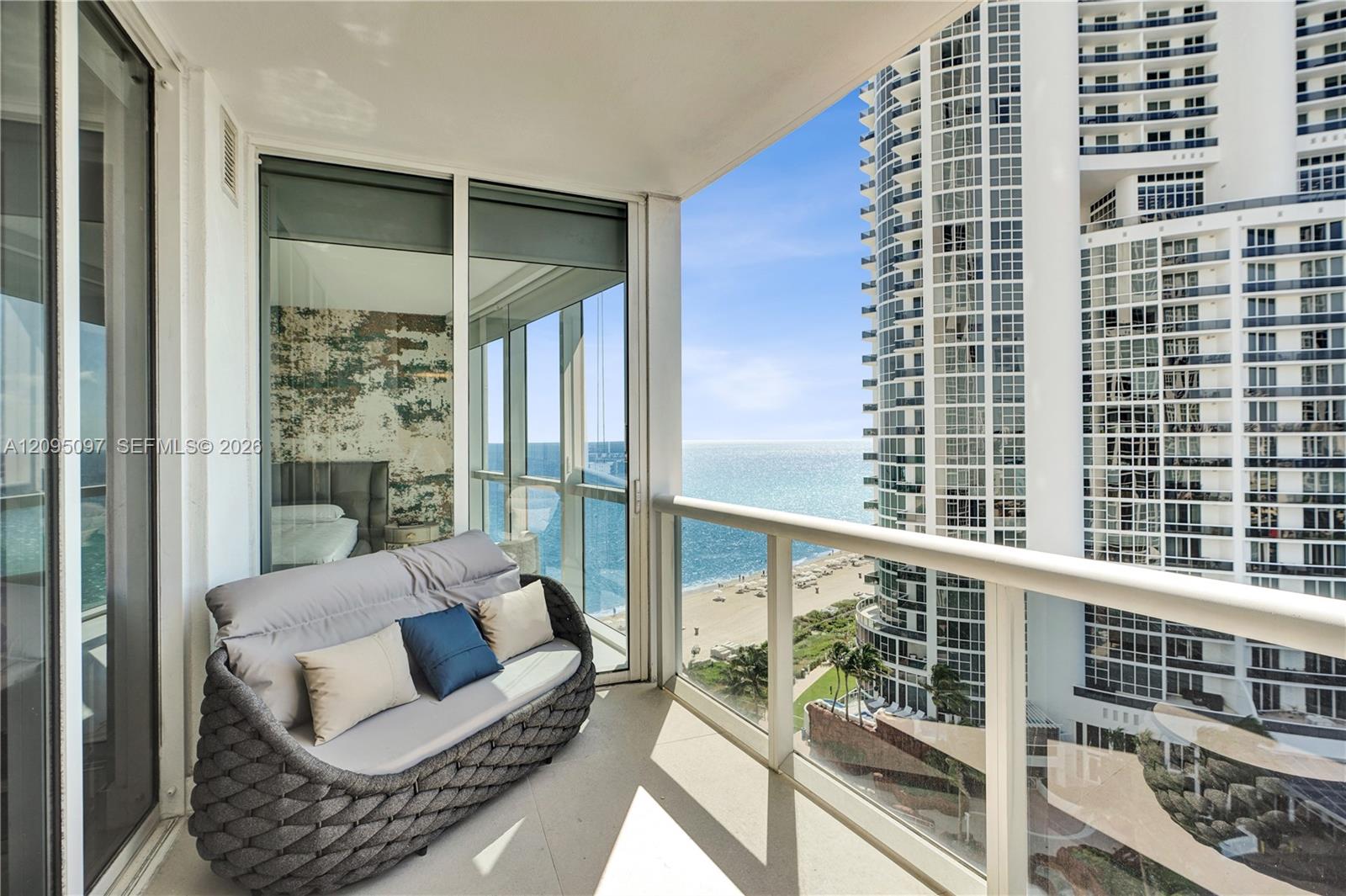 Covered private balcony featuring glass panel railings, floor-to-ceiling sliding glass doors, and panoramic ocean and coastline exposure