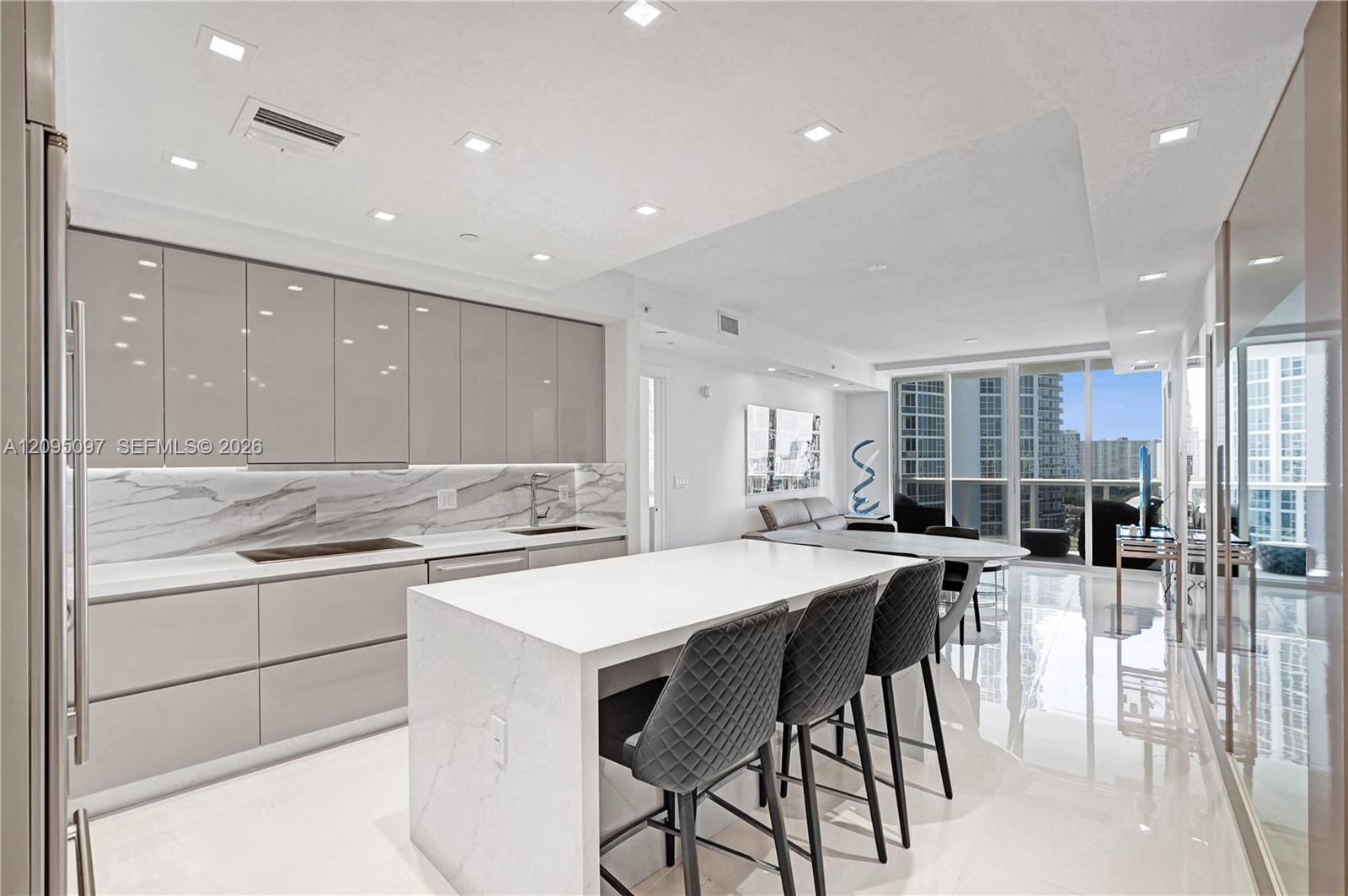 Contemporary kitchen featuring high-gloss cabinetry, a waterfall-edge stone island, stone-pattern backsplash, polished tile flooring, and recessed ceiling lighting