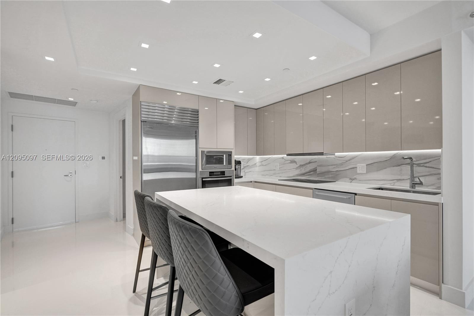 Contemporary kitchen featuring high-gloss cabinetry, a waterfall-edge quartz island, under-cabinet lighting, integrated stainless steel appliances, and stone-finish backsplash