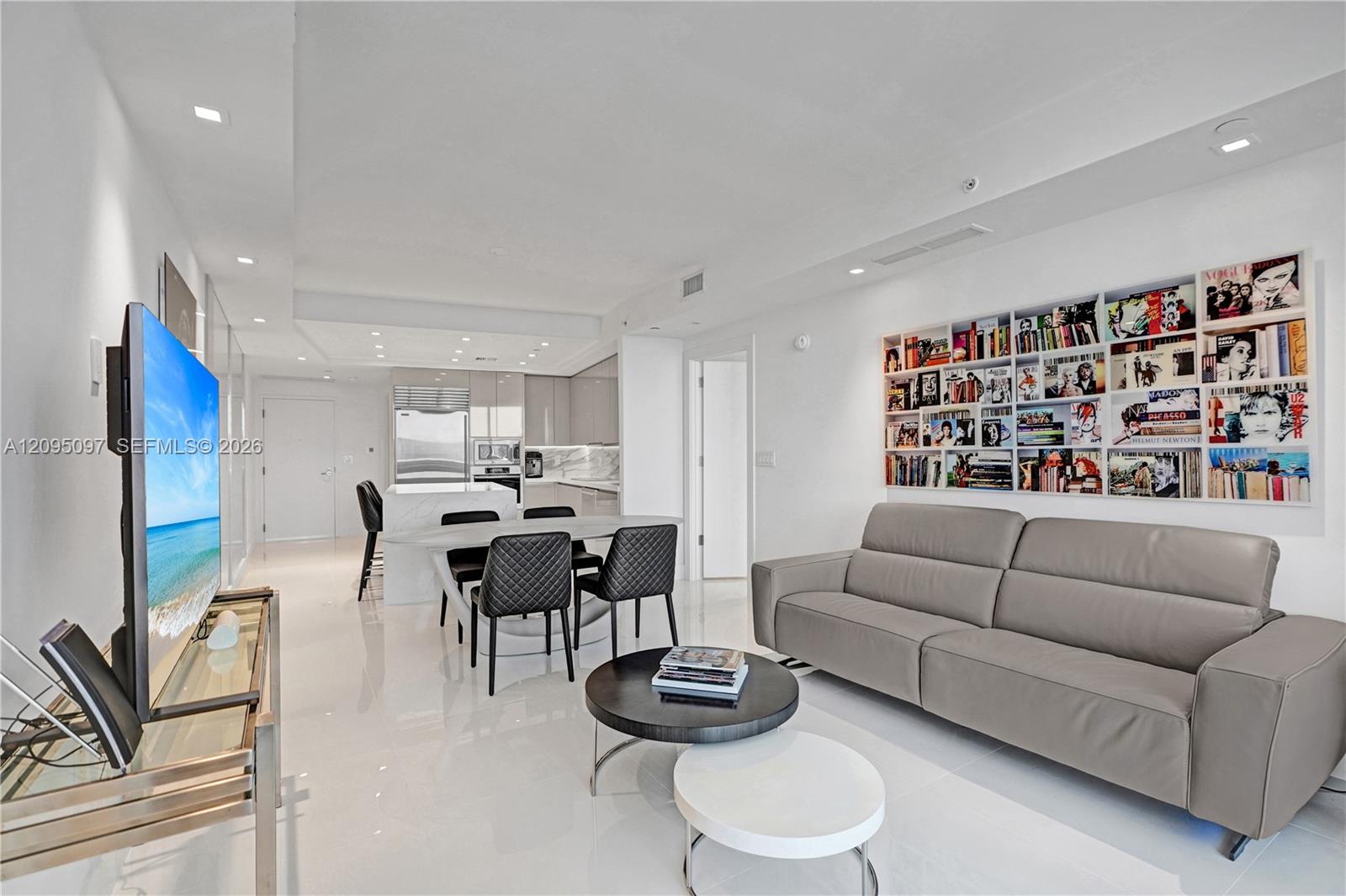Open-concept interior featuring high-gloss flooring, recessed lighting, a built-in recessed shelving unit, and a kitchen equipped with stone-surfaced countertops and stainless steel appliances
