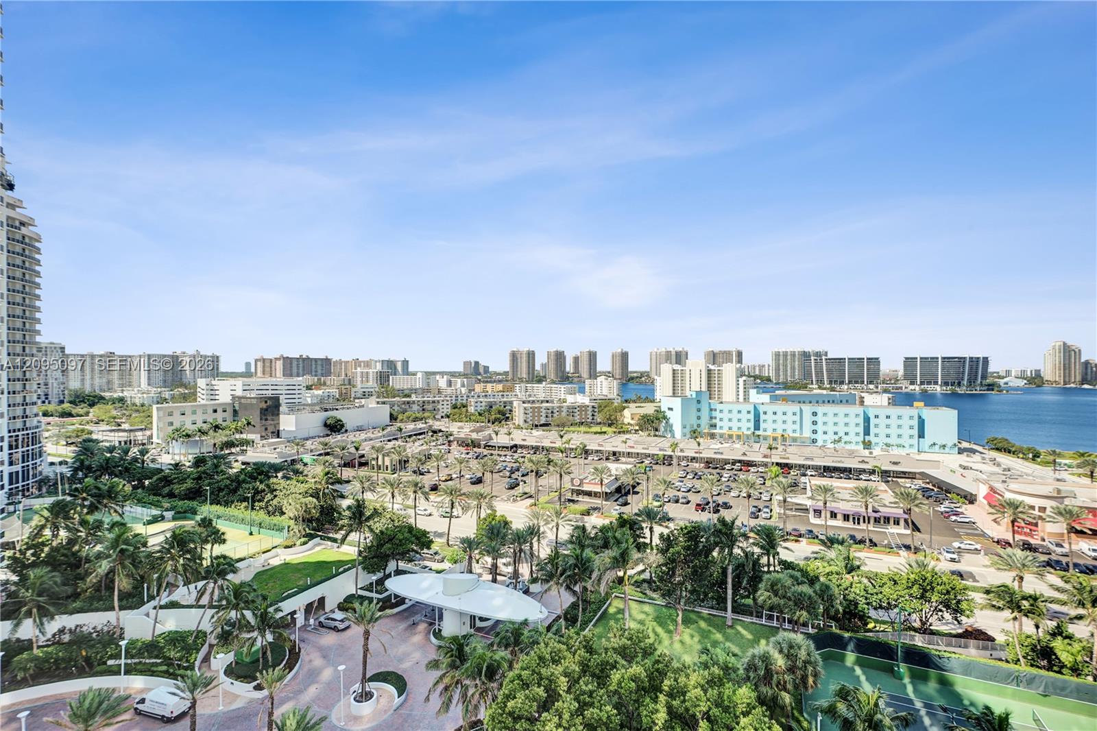 Elevated exterior perspective featuring a circular porte-cochre, paved motor court, mature landscaping, and tennis courts