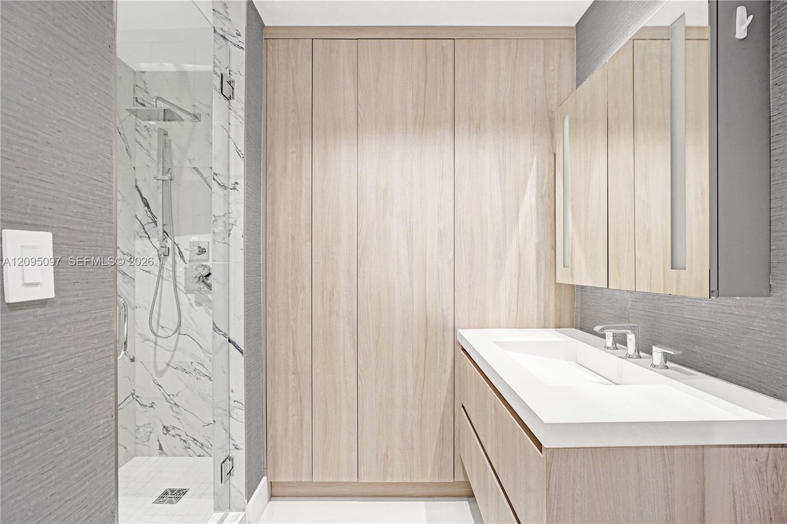 Bathroom featuring floor-to-ceiling wood-finish cabinetry, a floating vanity with an integrated basin, a walk-in shower with a rain-style showerhead, and wall-surround tile with a veined pattern