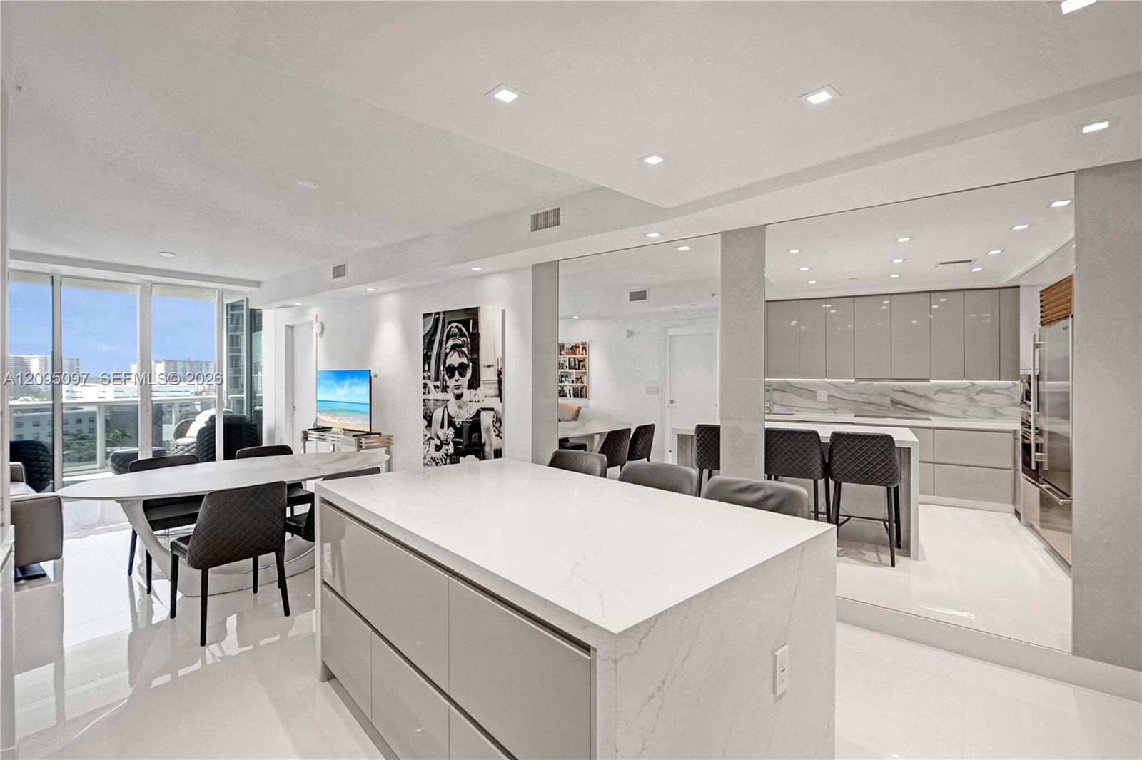 Open-concept interior featuring high-gloss cabinetry, a central island with a solid surface countertop, stone-finish backsplash, recessed ceiling lighting, and floor-to-ceiling windows