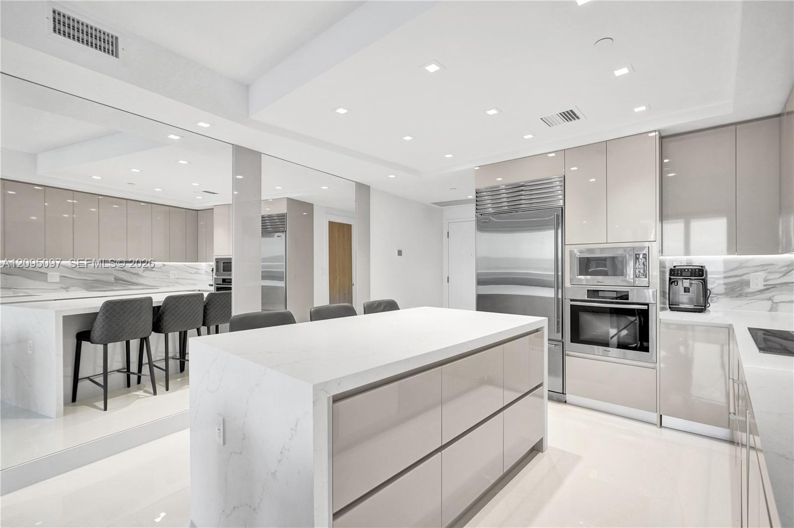 Modern kitchen featuring high-gloss cabinetry, stone-finish countertops with waterfall edge, integrated stainless steel appliances, and recessed ceiling lighting