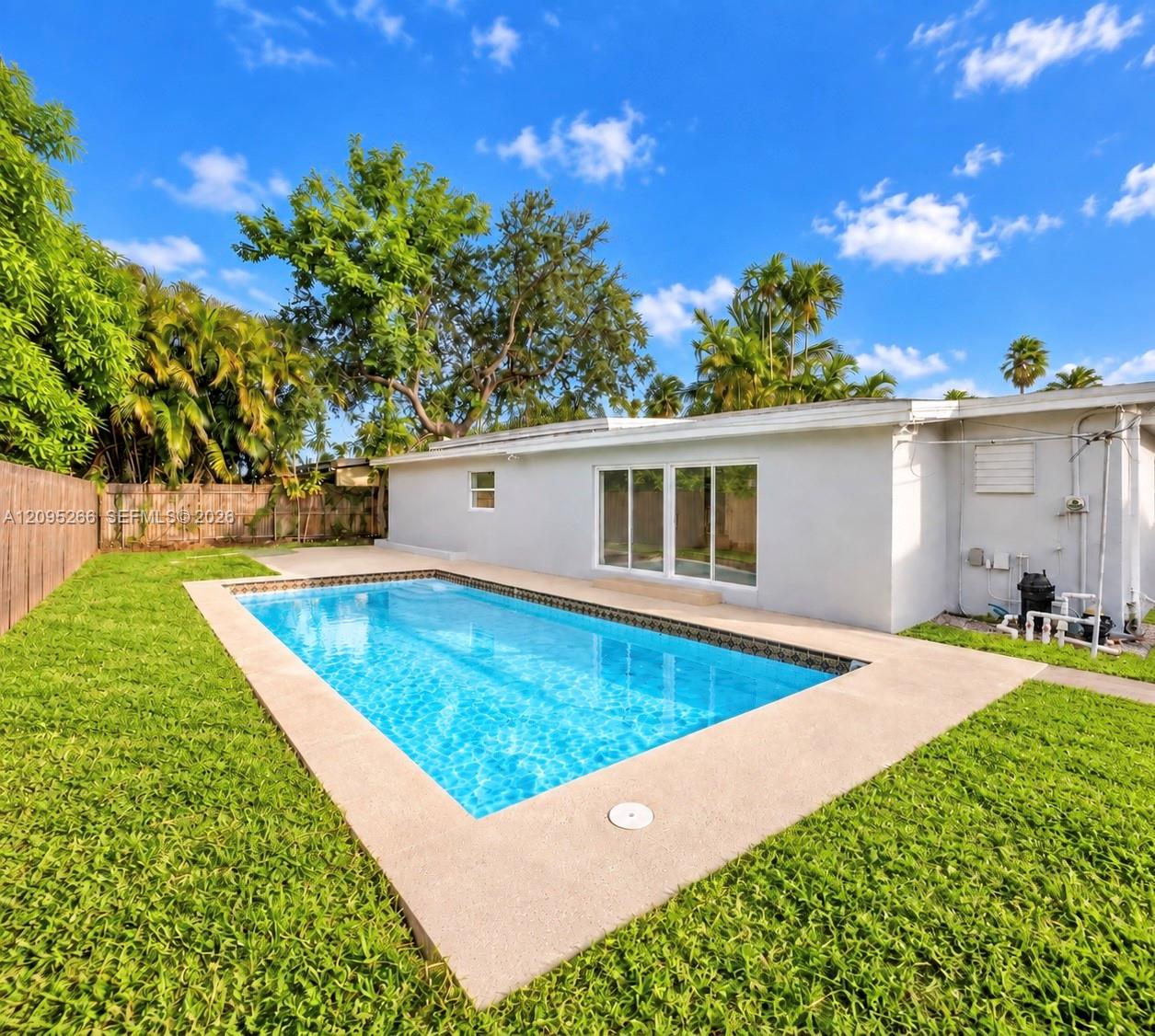 In-ground swimming pool featuring a concrete surround, enclosed by a privacy fence and accompanied by a lawn and mature trees