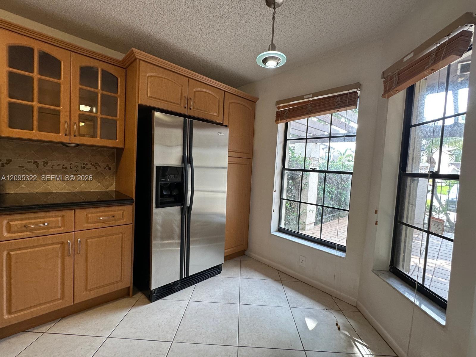 Kitchen featuring wood cabinetry with glass-front display panels, stainless steel side-by-side refrigerator, tile flooring, and dual windows with natural light