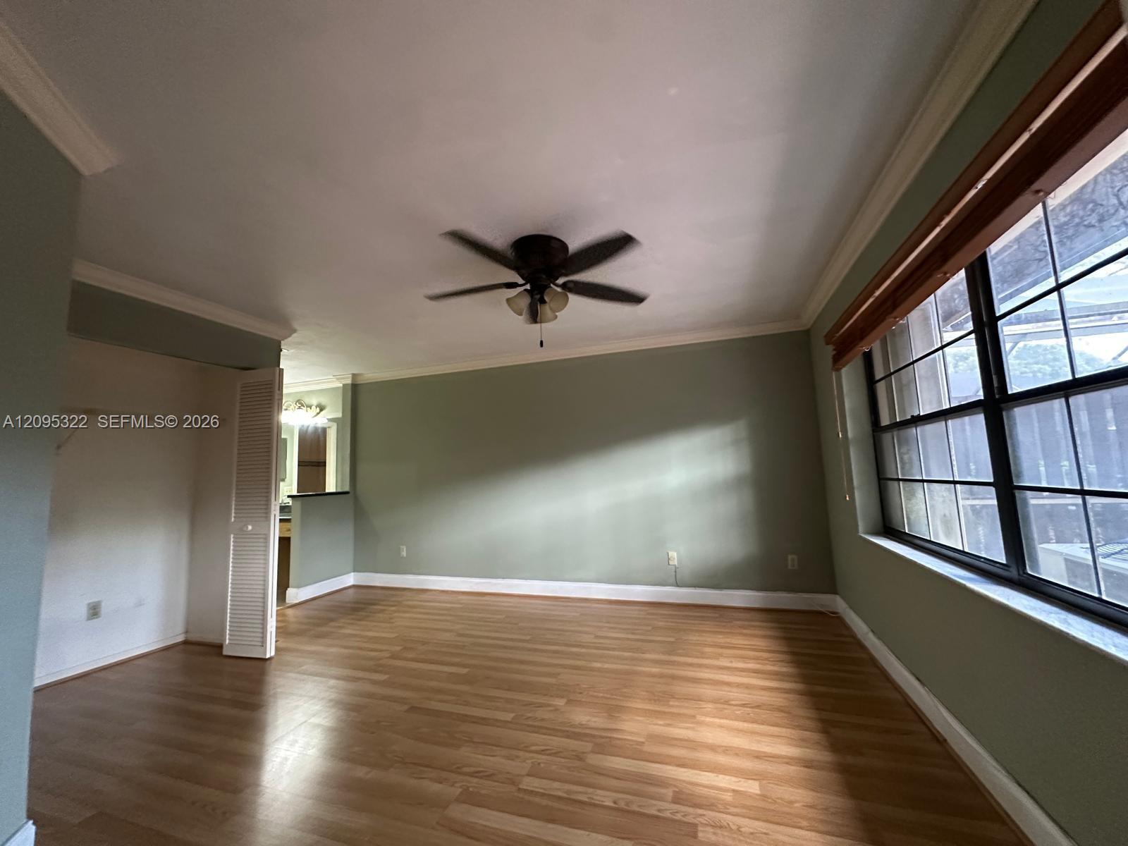 Room featuring wood-finish flooring, crown molding, a ceiling fan with integrated lighting, and multi-pane windows with wood-trim framing