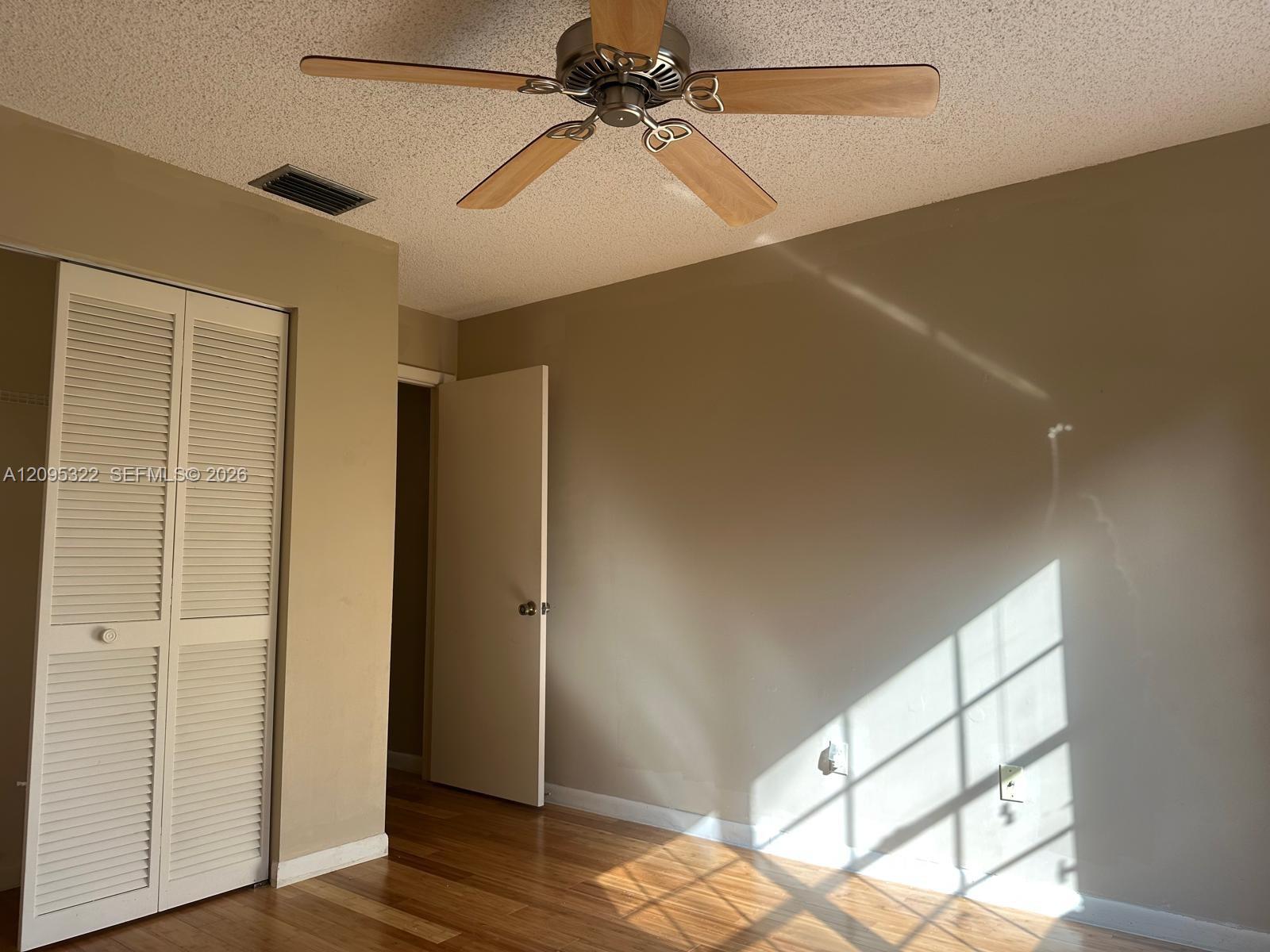 Wood-finish flooring, ceiling fan with wood-toned blades, and louvered double-door closet