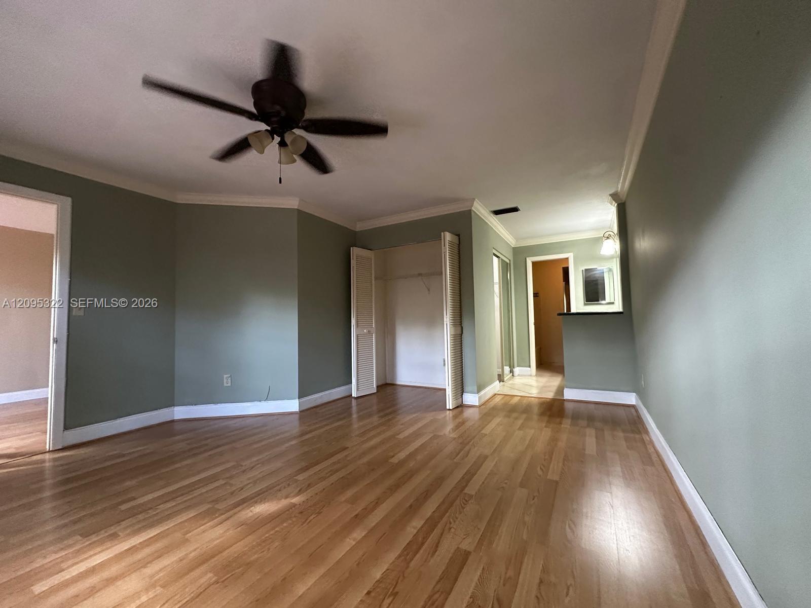 Interior space featuring wood-finish flooring, crown molding, a ceiling fan with integrated lighting, and a closet with bifold doors