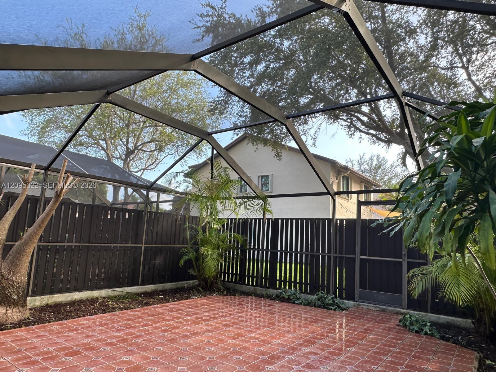 Screen-enclosed patio featuring decorative ceramic tile flooring, a dark-toned vertical slat privacy fence, and integrated landscaping