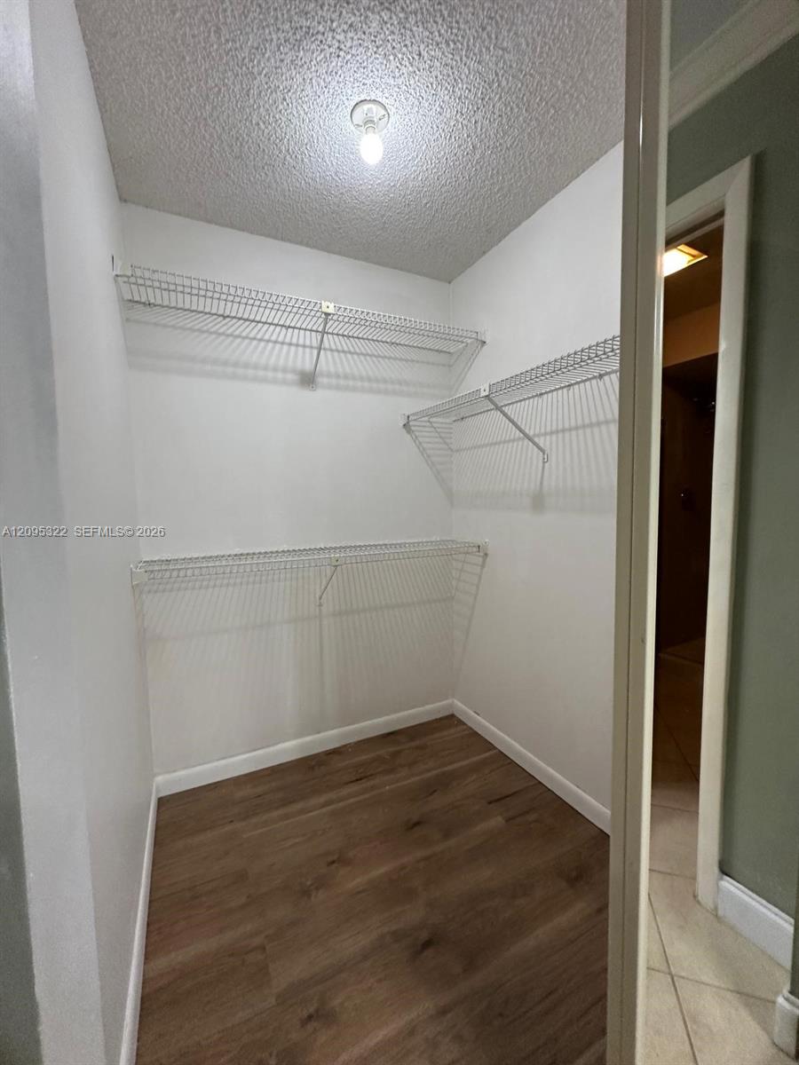 Storage closet featuring wood-finish flooring, white walls, and tiered metal wire shelving