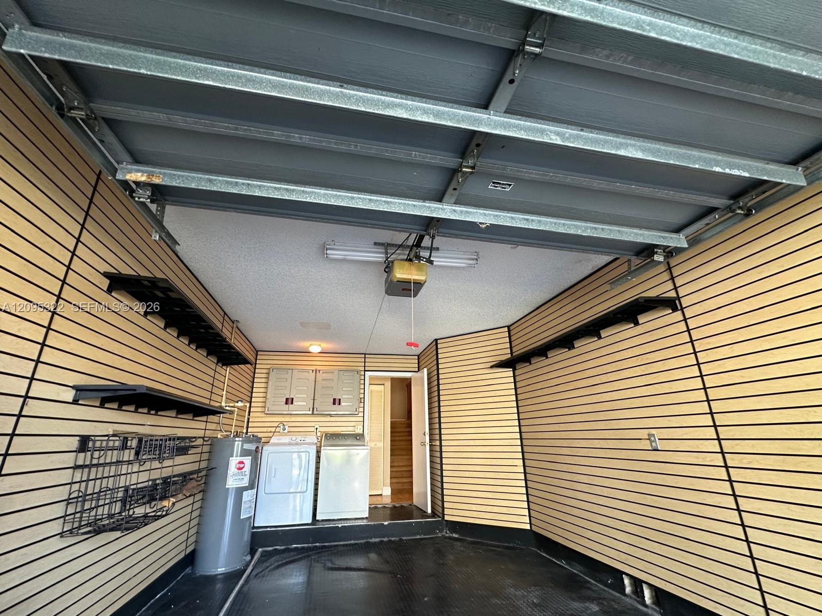 Garage interior featuring wall-mounted slat wall organizational panels, fixed shelving, a water heater, and built-in laundry hookups