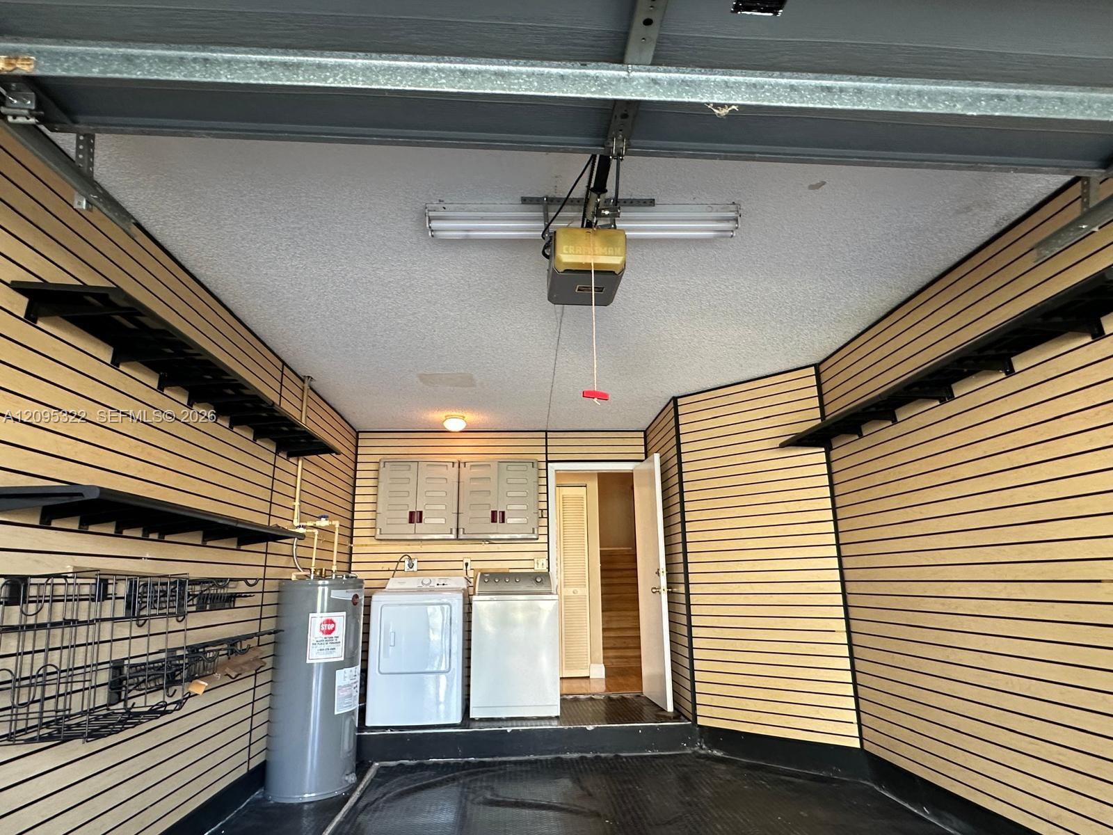 Garage featuring wall-mounted slat storage systems, fixed shelving units, upper cabinetry, and dedicated laundry area with integrated utility connections