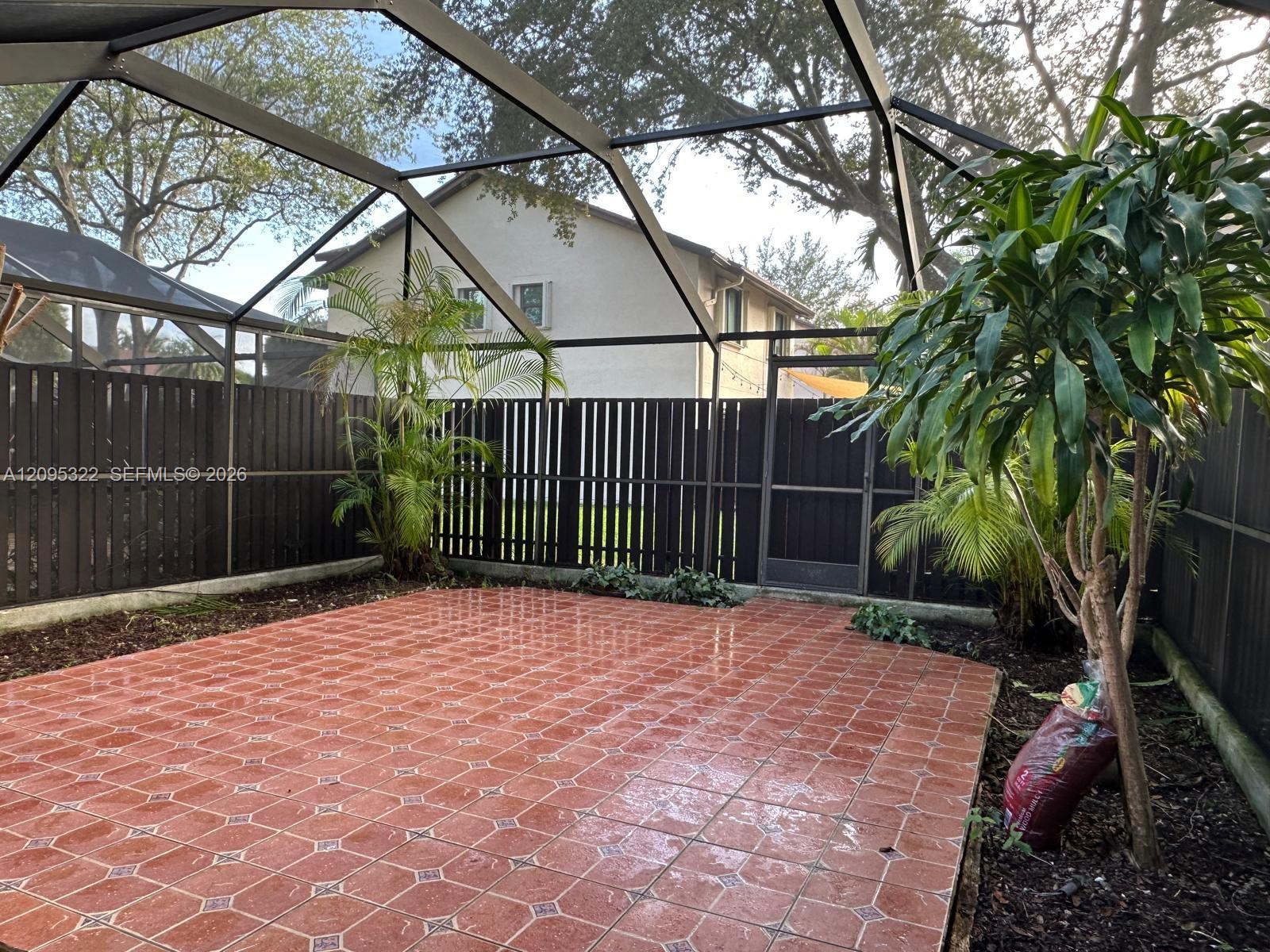 Enclosed outdoor patio featuring a screened-in roof, tiled flooring, wood-slat privacy fencing, and a built-in metal gate