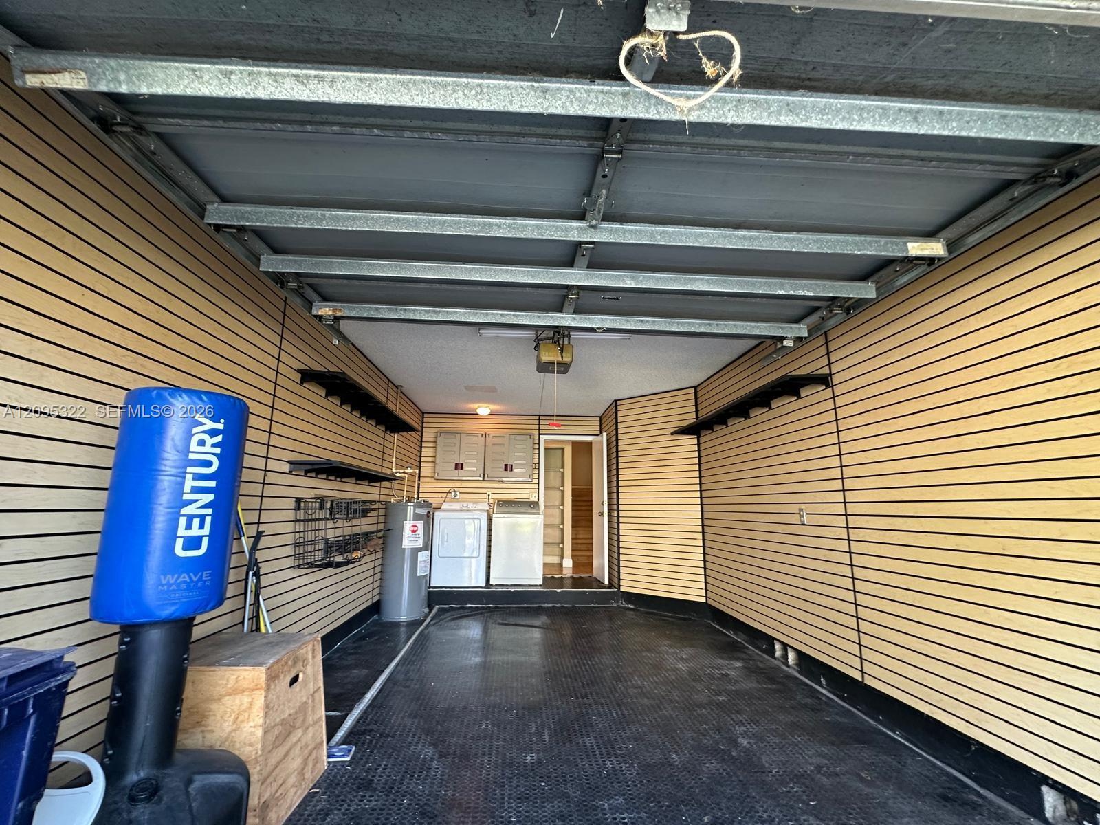 Garage interior featuring horizontal slat-wall paneling, rubberized textured flooring, integrated wall-mounted shelving, and laundry hookups