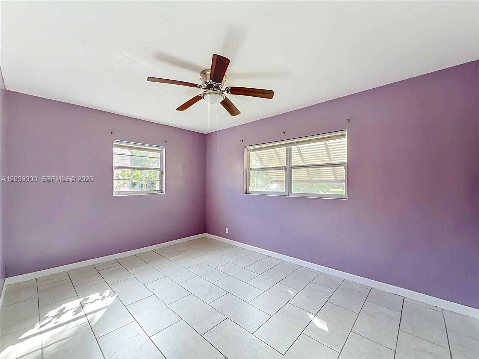 Interior room featuring large-format tile flooring, dual-aspect windows with metal horizontal blinds, and a central ceiling fan with integrated light fixture