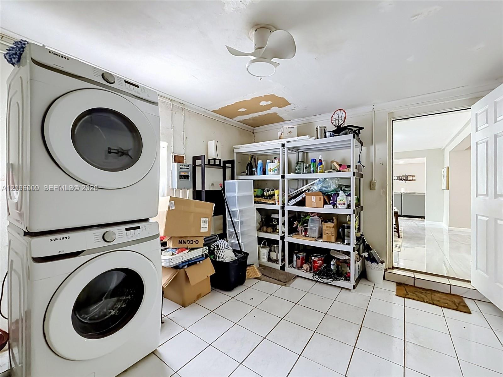 Utility area featuring white ceramic tile flooring, a ceiling-mounted fan, and a stacked front-load laundry appliance set
