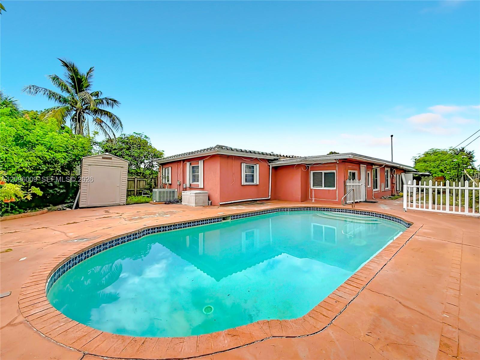 In-ground swimming pool with tile trim, expansive concrete patio, stucco exterior finish, and detached outdoor storage structure
