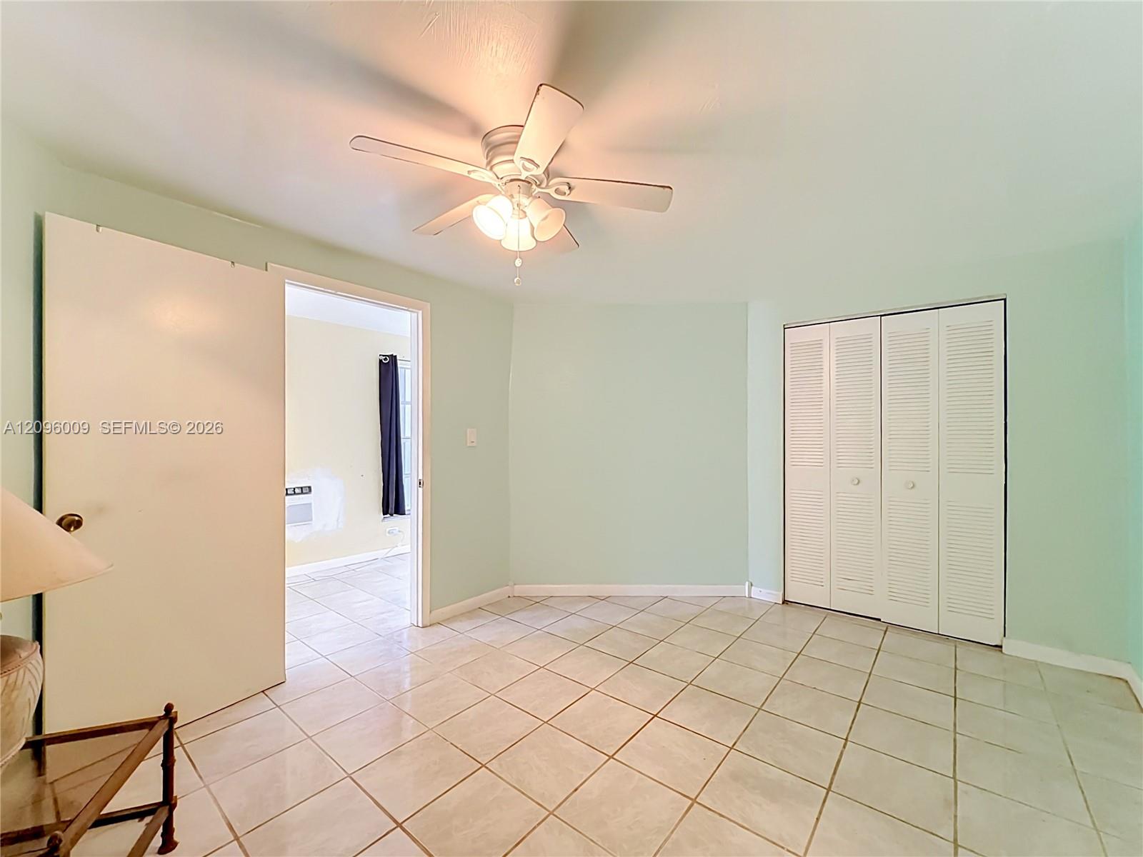 Tile flooring, light-toned wall paint, white louvered-door closet, and ceiling fan with integrated lighting