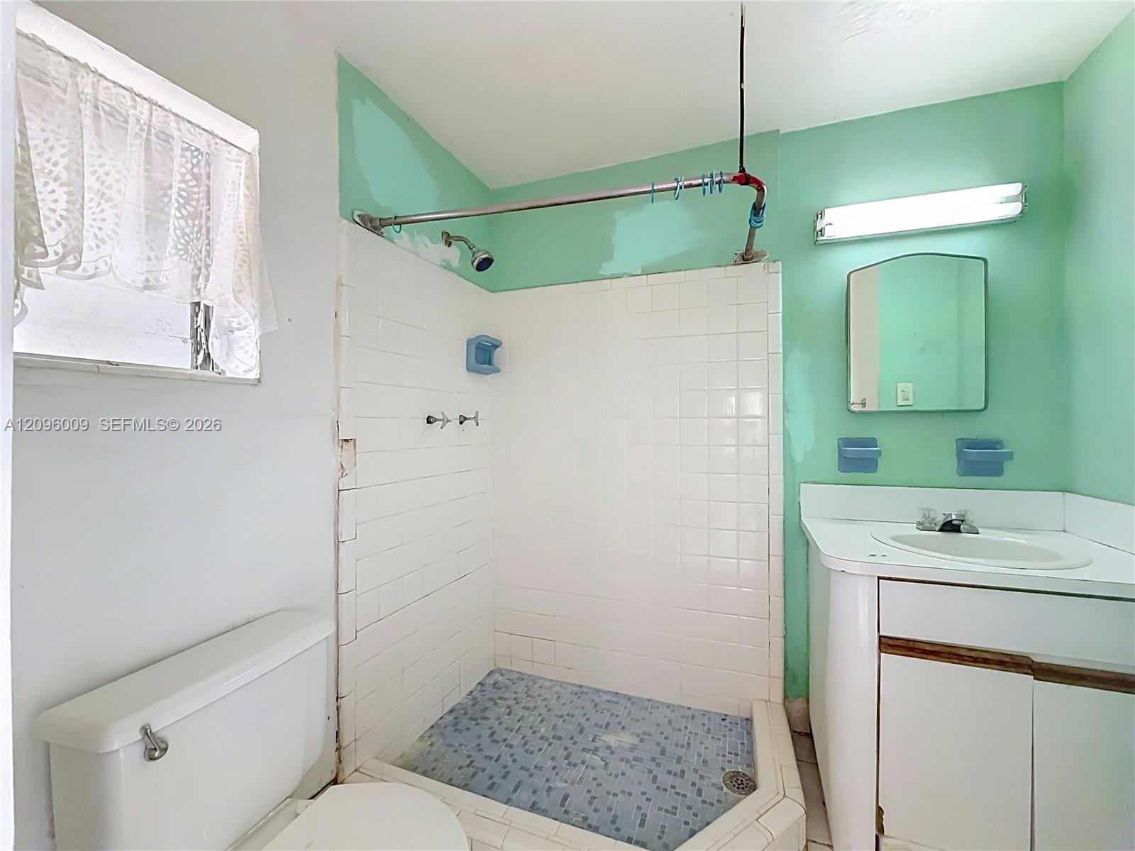Bathroom featuring a tiled shower enclosure, white vanity cabinet with a drop-in sink, wall-mounted mirror, and overhead light fixture