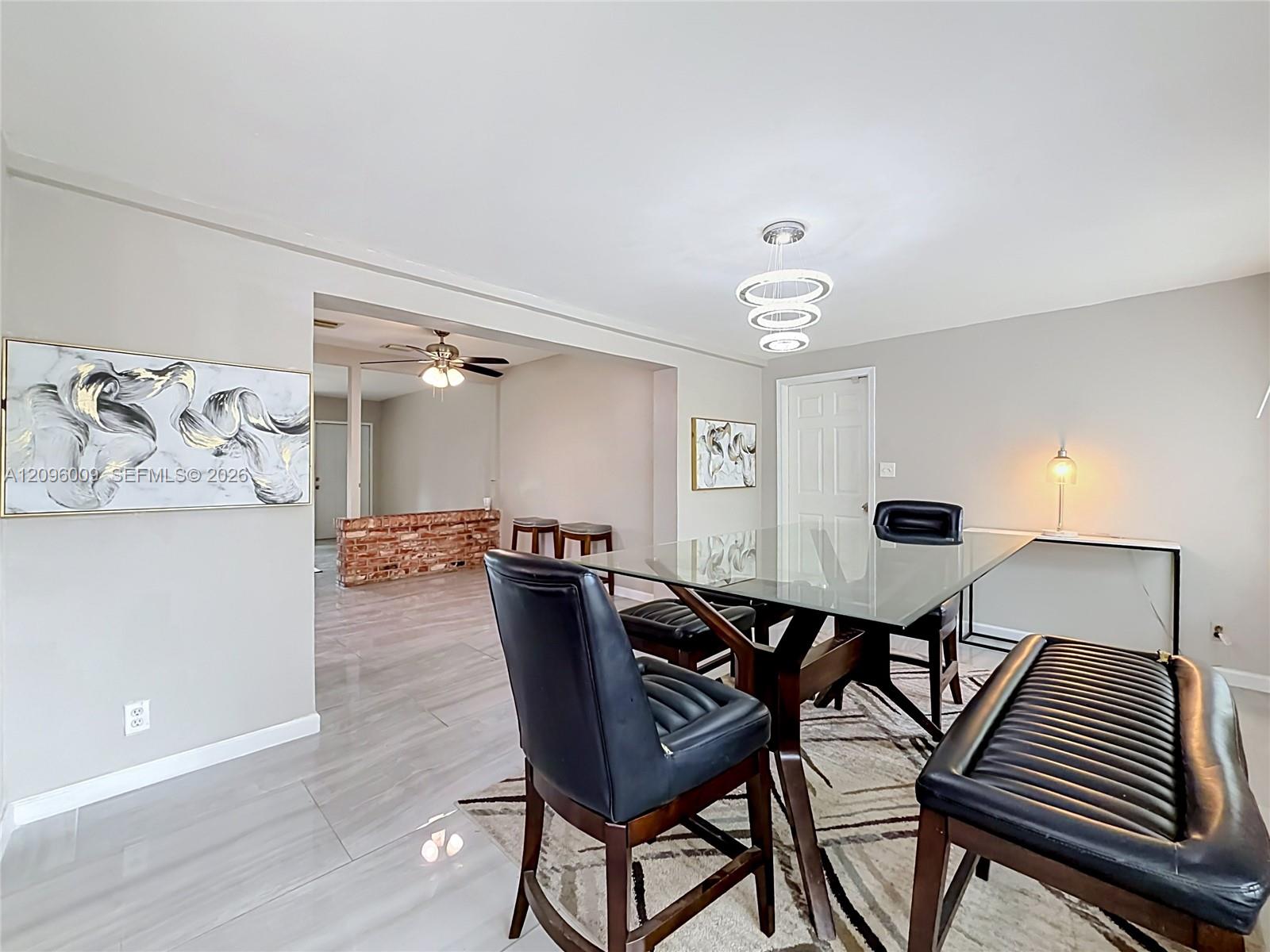 Large-format tile flooring, modern tiered circular chandelier, decorative brick accent wall, and six-panel interior door