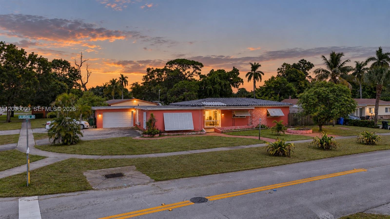 Single-story residence featuring a stucco exterior, attached two-car garage, metal awning accents, and landscaped lawn with mature palm trees