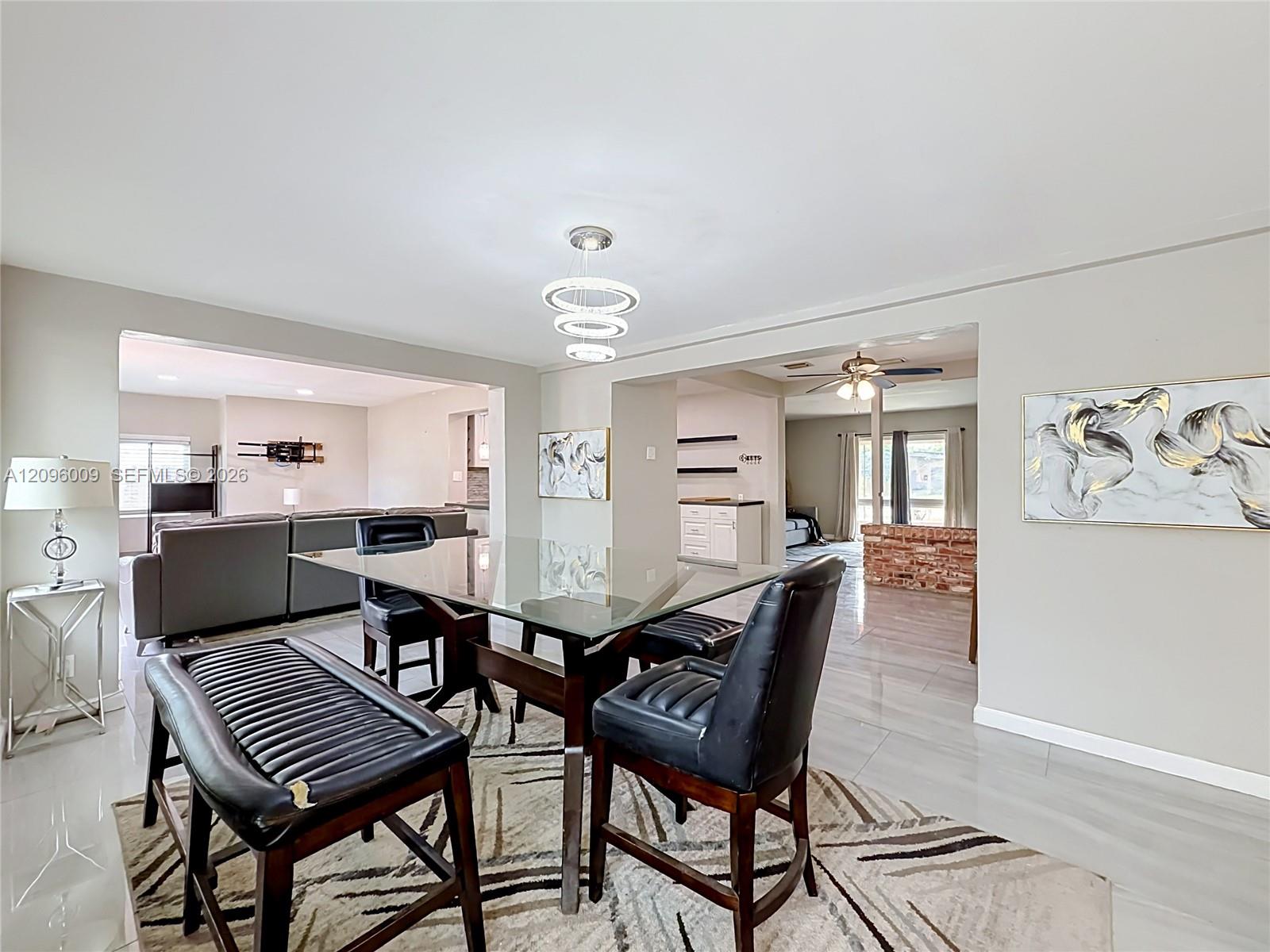 Open-concept dining area featuring neutral wall tones, large-format tile flooring, a multi-tiered circular pendant light fixture, and a brick partition wall