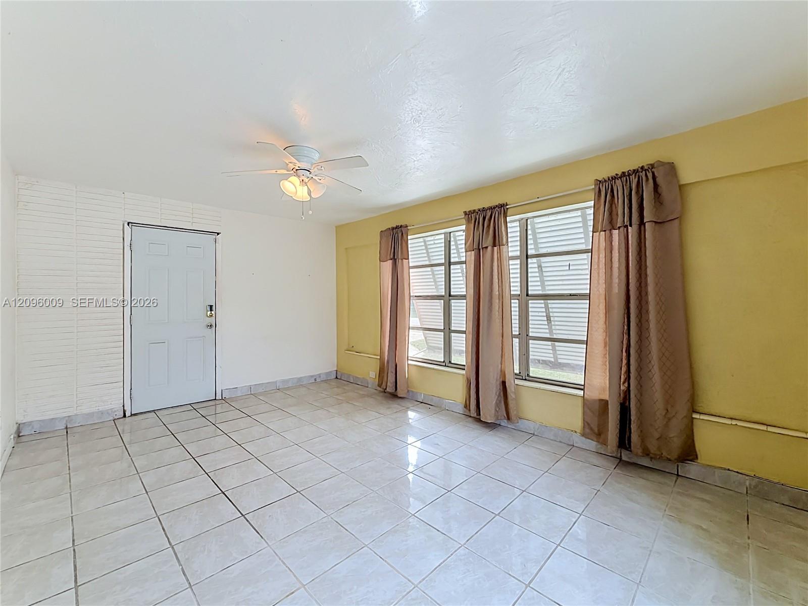 Interior space featuring ceramic tile flooring, a painted brick accent wall, and a central ceiling fan with integrated lighting