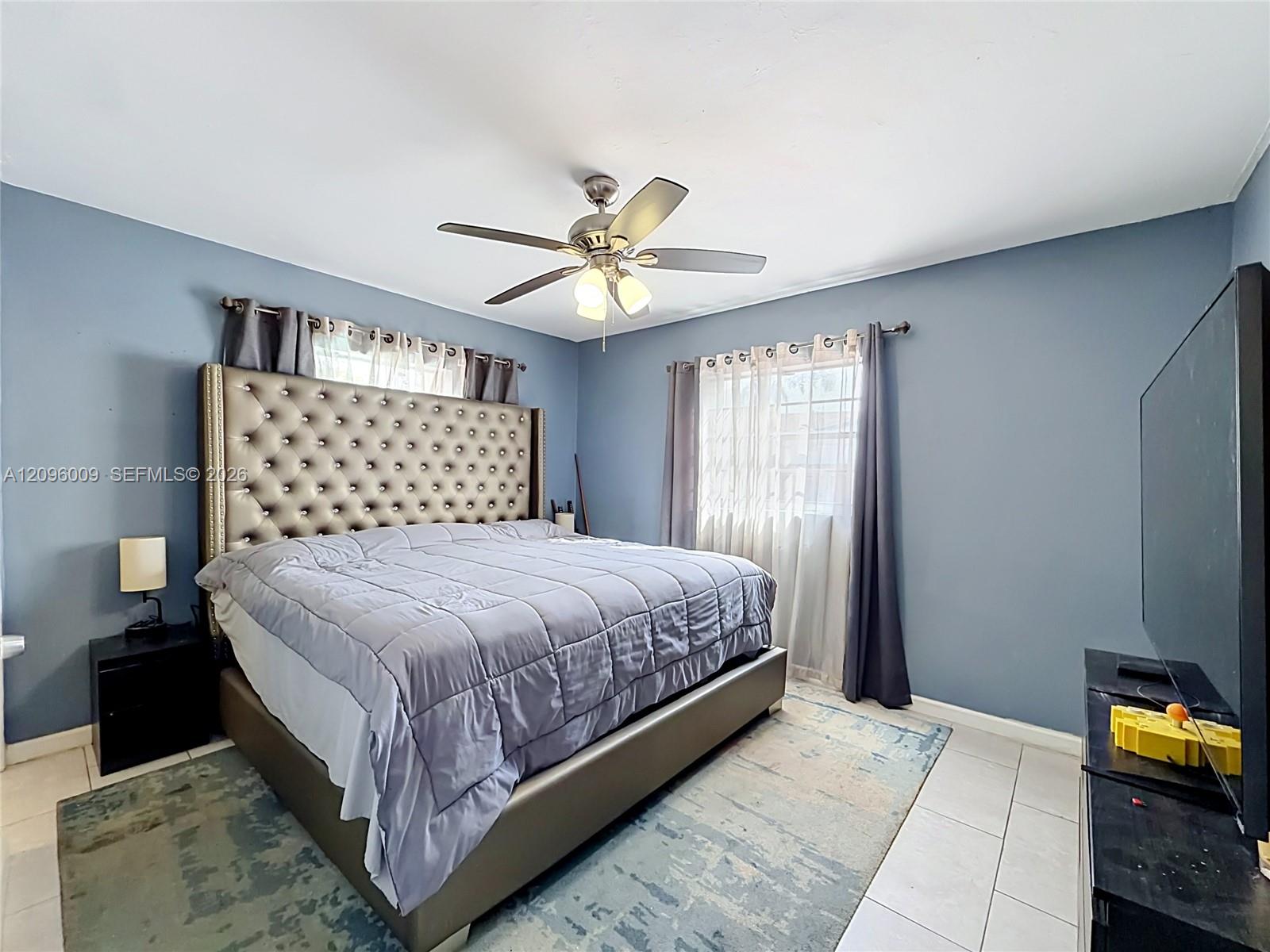 Light-filled room featuring large windows with neutral-toned treatments, tile flooring, and a ceiling-mounted light fixture with a central fan