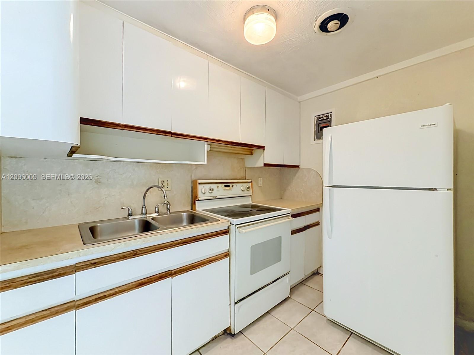 Kitchen featuring white cabinetry, a dual-basin stainless steel sink with a high-arch faucet, a white electric range, a white refrigerator, and tiled flooring