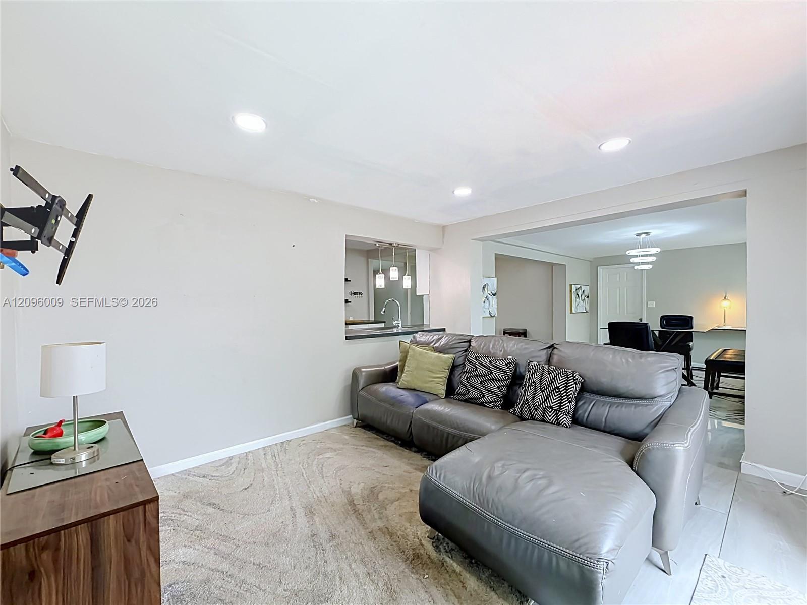Living area featuring neutral-toned walls, recessed lighting, and a pass-through window to the kitchen