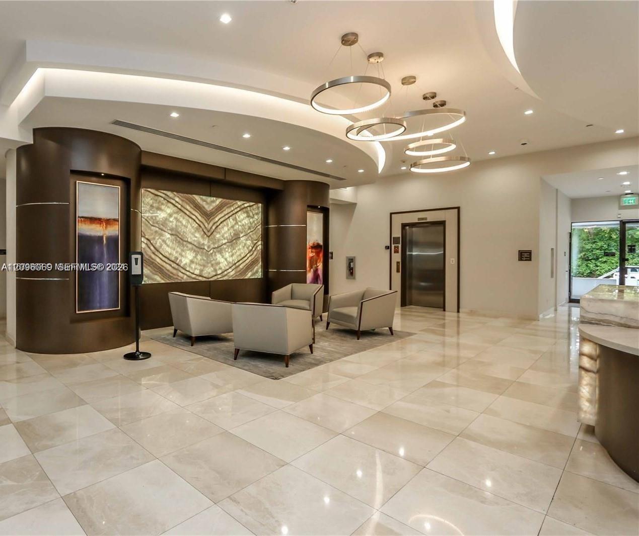 Lobby featuring large-format tile flooring, a curved architectural wall accent, backlit stone wall paneling, modern tiered circular pendant lighting, and recessed cove lighting