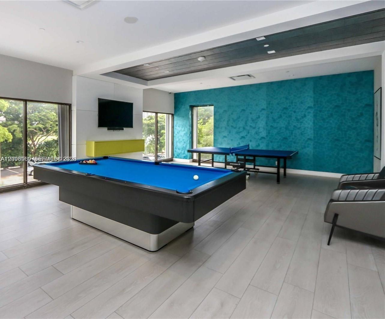 Recessed ceiling featuring dark-toned plank detailing, wood-finish flooring, floor-to-ceiling glass windows, and a textured teal accent wall
