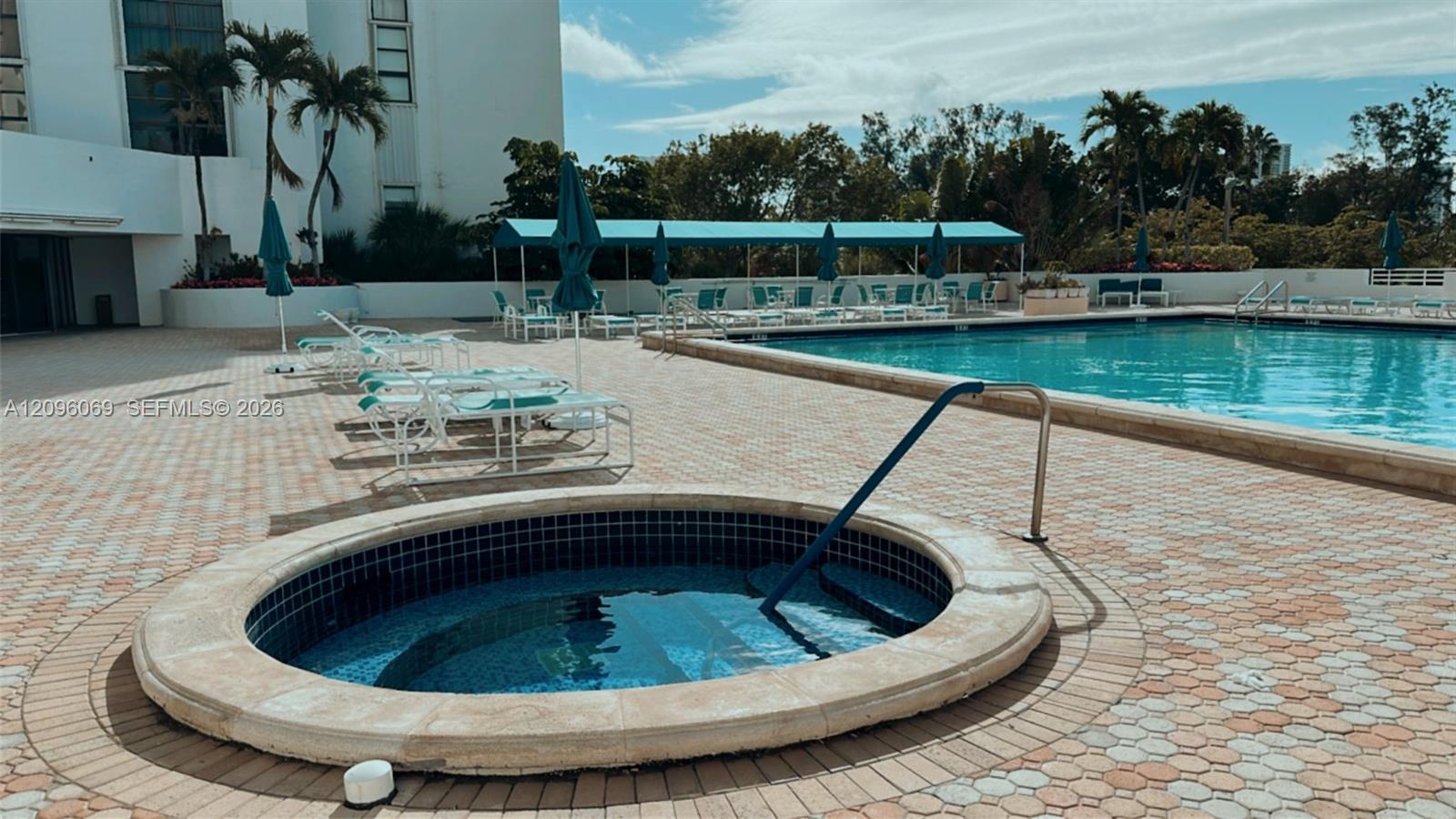 In-ground pool and circular spa featuring tile finishes, metal safety railings, and brick-patterned paved decking
