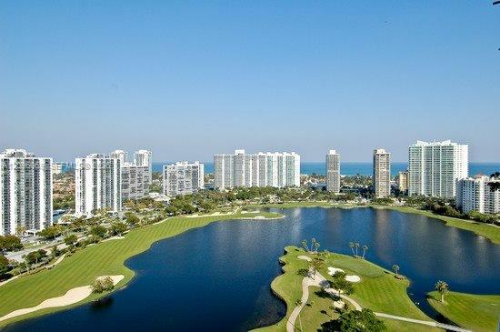 Panoramic aerial perspective featuring a golf course, expansive lake, and high-rise skyline